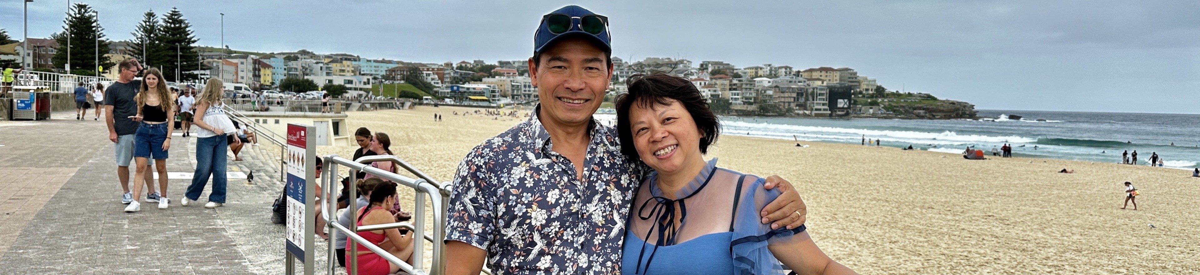 A couple smiling for a photo on the sandy beach, with the ocean in the background.