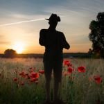 A man stands in a poppy field, his silhouette contrasting against the vibrant red flowers