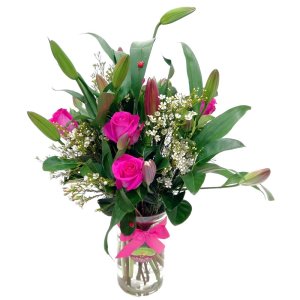 A flower arrangement featuring a vase filled with pink roses, pink lilies, pink tulips and white wax flowers